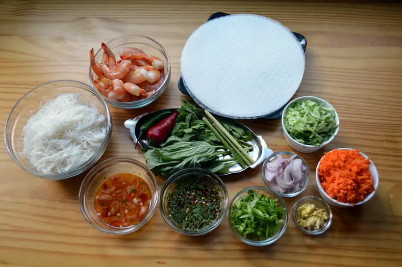 View of ingredients - grated carrot, onions, shrimps, chili pepper, garlic, vermicelli noodles, cucumbers, basil, rice paper rolls