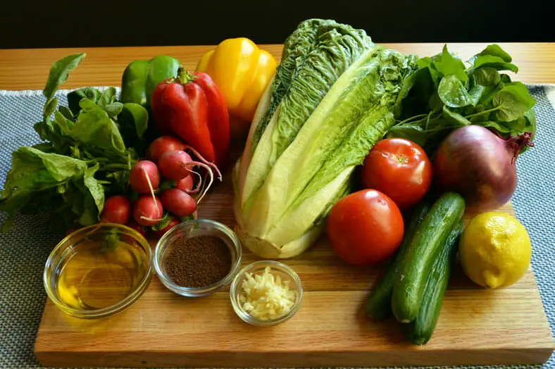 View of ingredients - onions, lemon, tomatoes, Romaine lettuce, purslane, cucumbers, red, yellow and green bell peppers, radishes, garlic