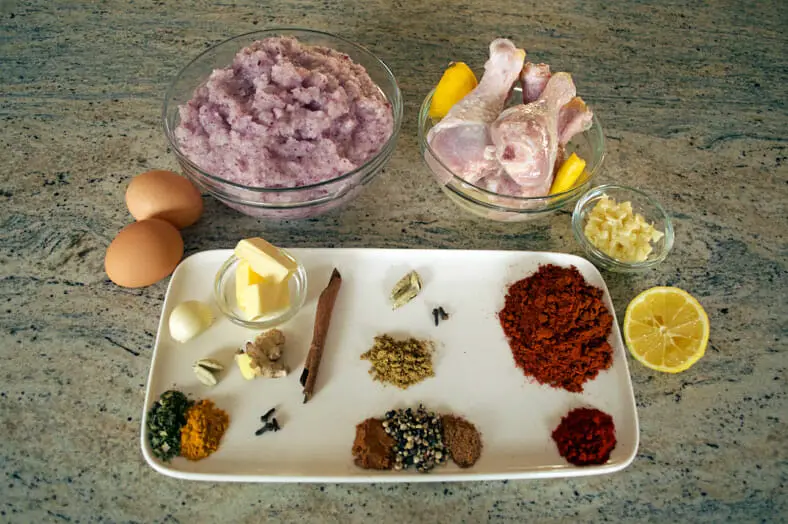 View of ingredients - lime, butter, spices, cinnamon stick, garlic, eggs, chicken, chopped onions 