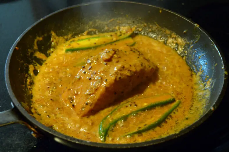 The salmon simmering and essentially poaching in the yellow shorshe fish curry sauce