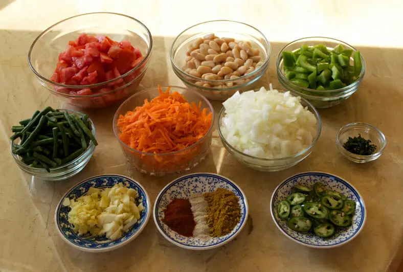 View of ingredients - tomatoes, onions, bell peppers, spices, garlic, green beans, coconut oil, thyme