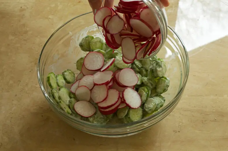 Adding cucumber and radish to the dressing bowl