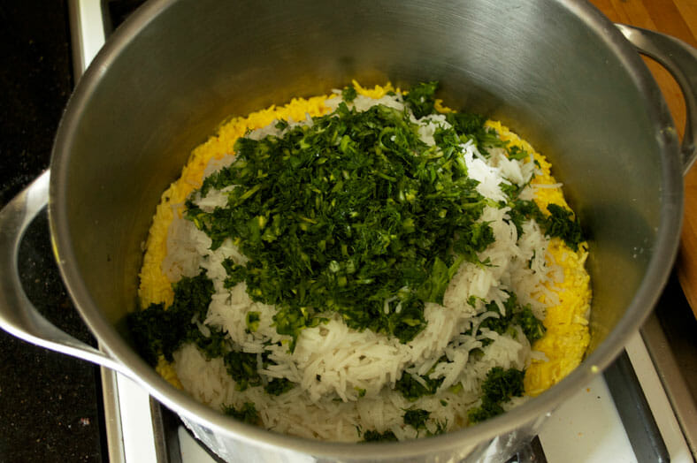 Adding chopped herbs to the rice in pot