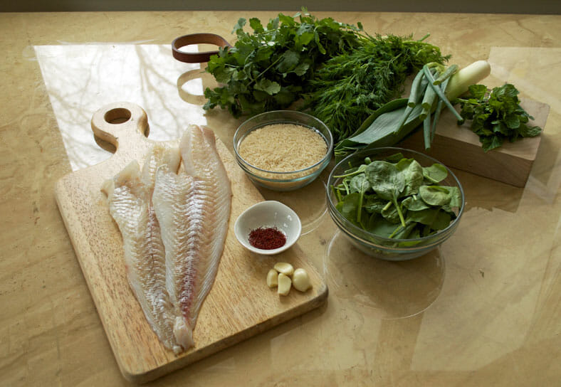 View of ingredients - fish, rice, garlic cloves, spring onions, parsley, dill, coriander, mint
