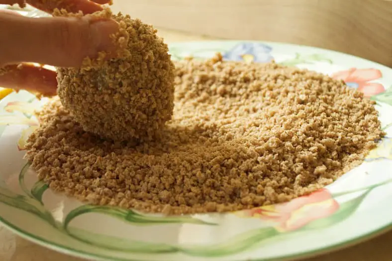Rolling meat encased boiled egg into breadcrumbs for coating
