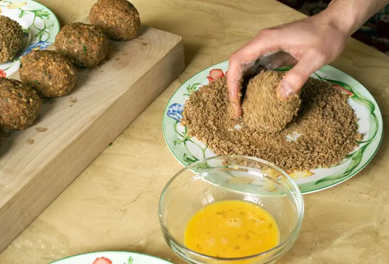 Rolling sausage boiled egg into breadcrumbs
