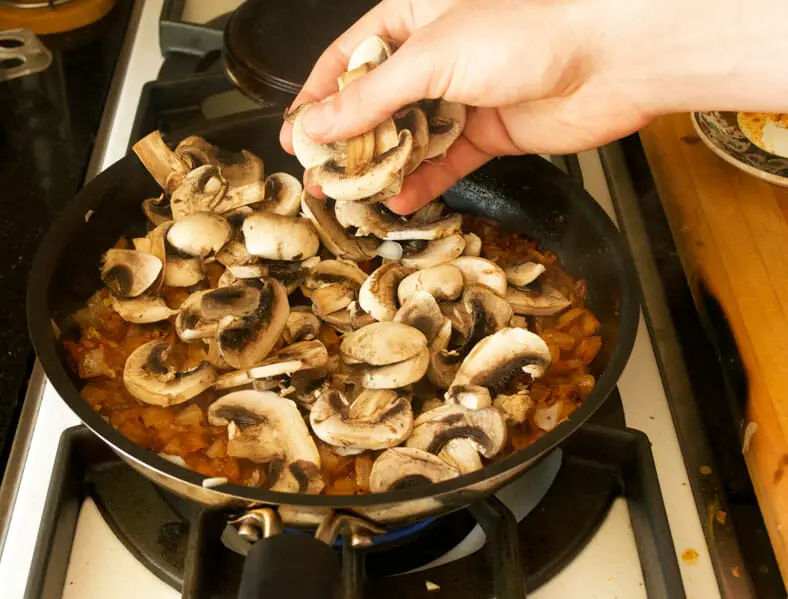 Adding mushrooms to the spices and onions to the vegetarian filling