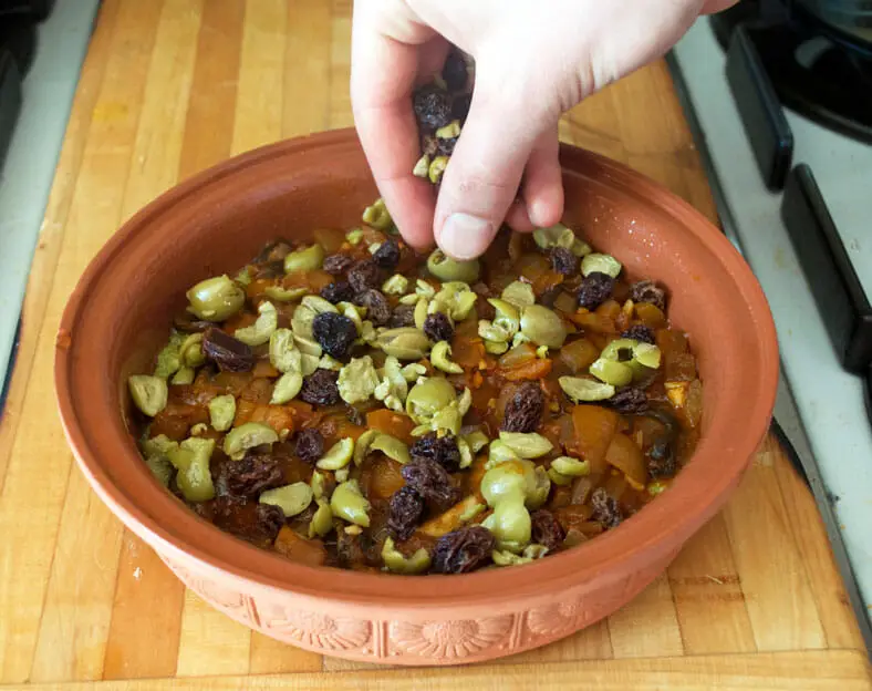 Sprinkling olives and raisins over the vegetarian mushroom and onion filling for the Chilean pastel de choclo (corn pie)