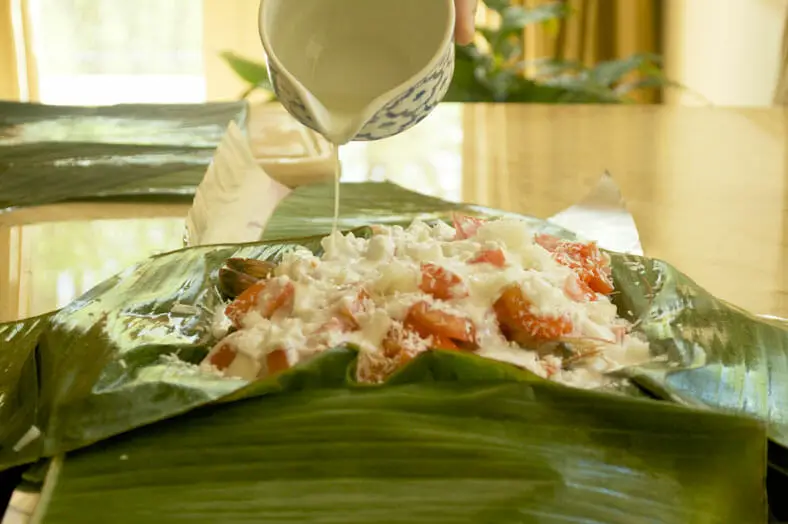 Pour lime juice into a banana leaf stuffed with yam onion prawns and tomato for the dish
