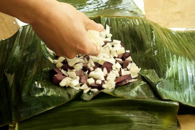 Stuffing a banana leaf with yam and onion for the curry dish