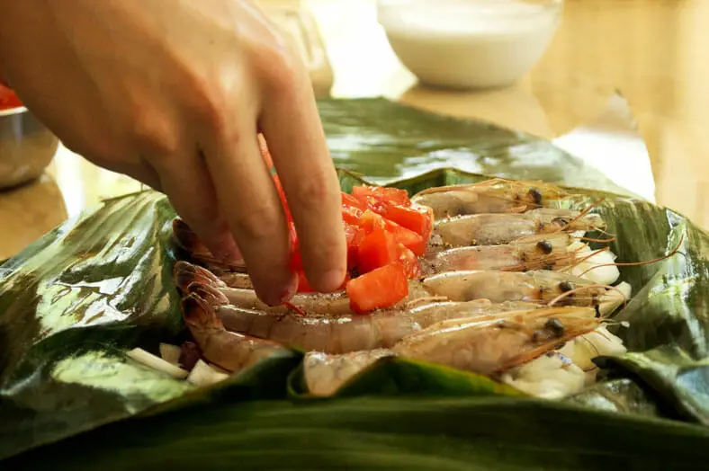 Stuffing a banana leaf with yam onion prawns and tomato for curry