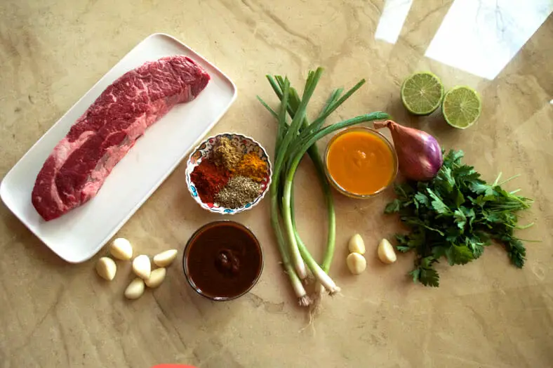 View of ingredients - lemons, shallots, garlic, spring onions, spices, tomato sauce, aji panca paste, beef, cilantro