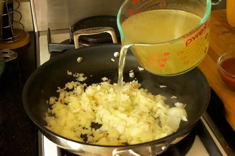Vegetable broth being added to sauteed onions for Zimbabwe Dovi (Peanut Stew)