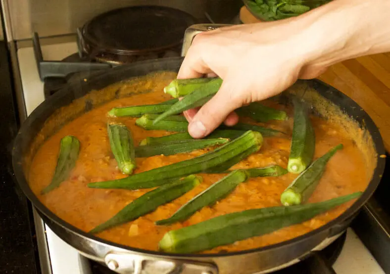 Adding okra to the simmering peri peri sauce, sauteed onions, carrots, tomato sauce and peanut butter