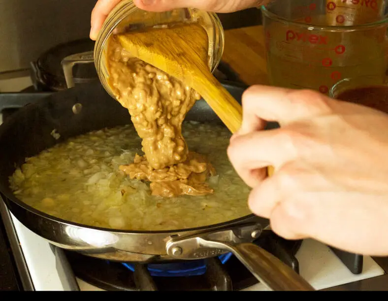 Peanut butter being added to sauteed onions and vegetable broth for Zimbabwe Dovi (Peanut Stew)