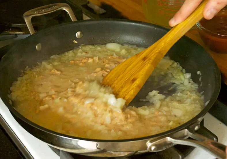 Mixing together peanut butter, sauteed onions and vegetable broth 