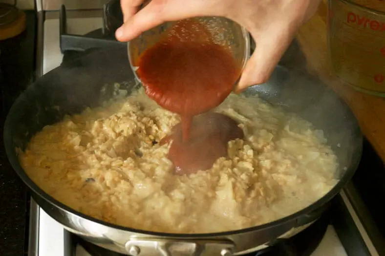 Tomato sauce being added to peanut butter, sauteed onions and vegetable broth for Zimbabwe Dovi (Peanut Stew)