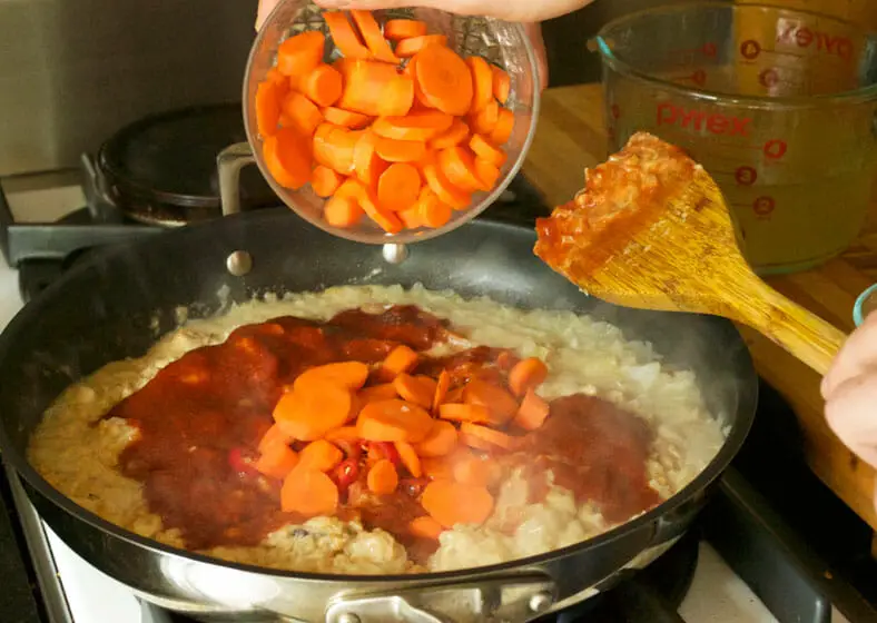 Carrots being added to tomato sauce, peanut butter, sauteed onions and vegetable broth for Zimbabwe Dovi (Peanut Stew)