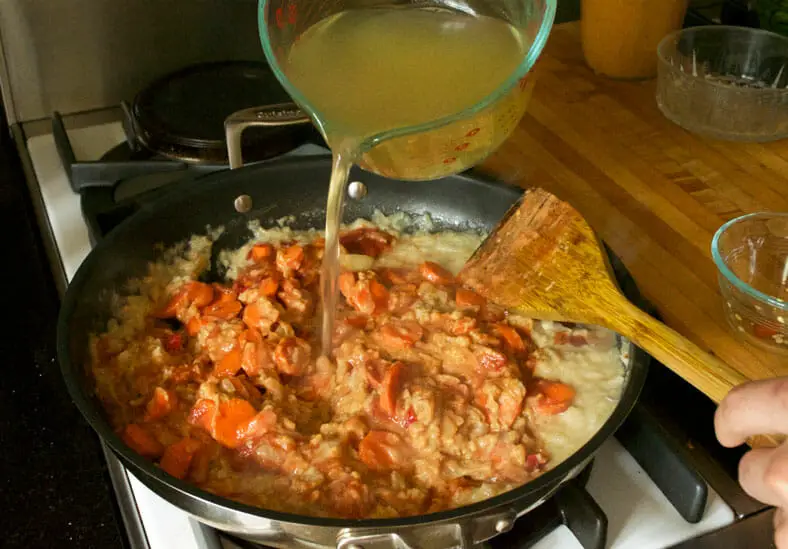 Vegetable broth being added to sauteed onions, carrots, tomato sauce and peanut butter for Zimbabwe Dovi (Peanut Stew)