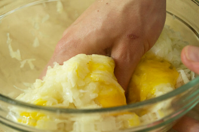Mixing eggs with grated onions and potato with hands