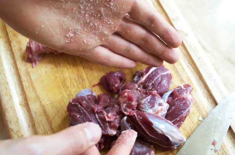 Hand Seasoning Lamb with salt and pepper on a wooden cutting board for dish
