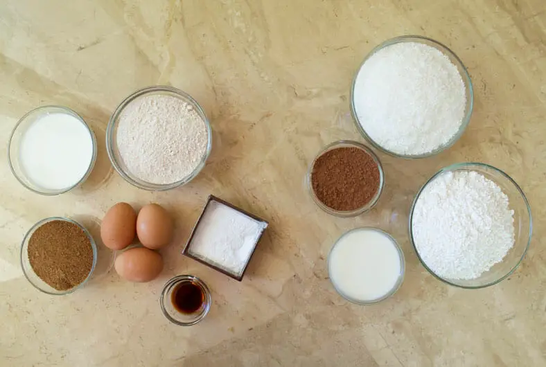 View of ingredients - coconut flakes, brown sugar, flour, eggs, vanilla extract, butter, baking powder