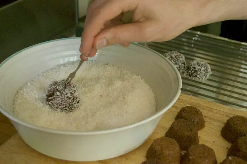 Rolling chocolate covered sponge cake into coconut flakes for proper sticking