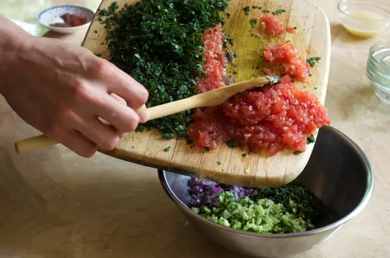 adding tomato and parsley to red onion, cucumber and mint for the Syrian Tabouli salad