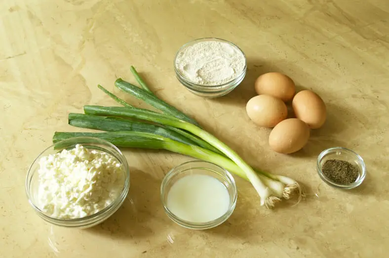 View of ingredients - cottage cheese, a mixture of buckwheat and pastry flour, milk and some whipping cream, four whole eggs, some black pepper, and scallions