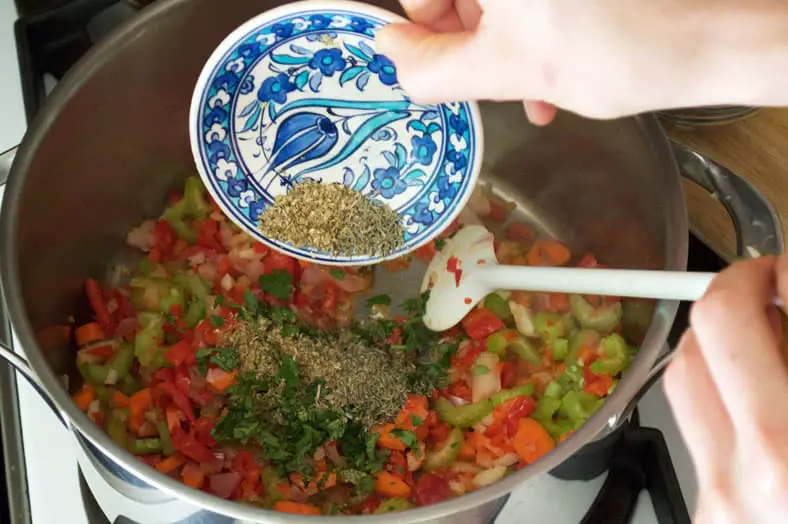 Adding dry herbs to pan for sazón