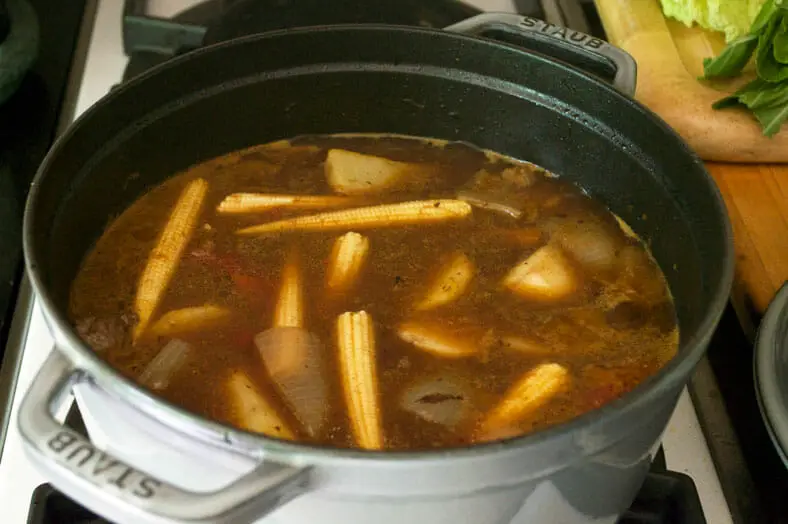 Adding baby corn into the beef stewing with tomatoes, onions, garlic and ginger