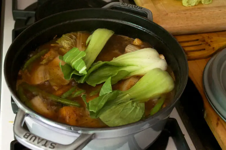 Top stew with baby bok choy over pan