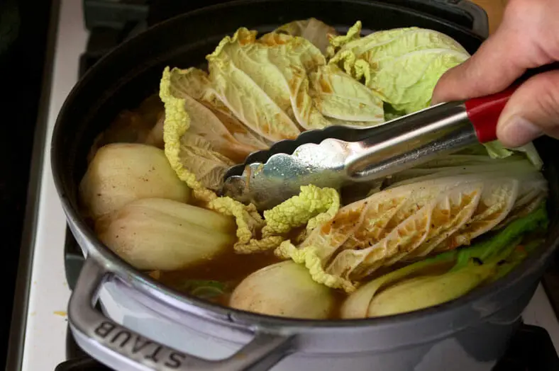 To finish pochero, a Filipino pork stew, top the stew with leaves of cabbage
