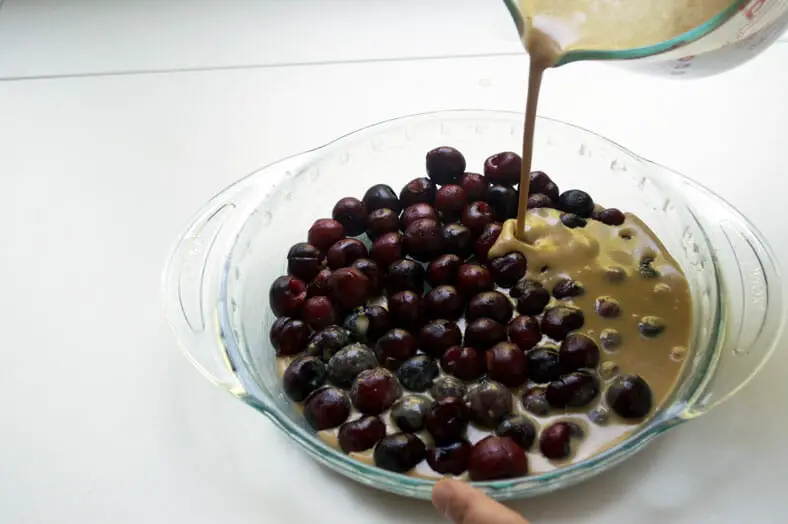 Pouring the batter over the cherries for a French clafoutis or a cherry custardy tart