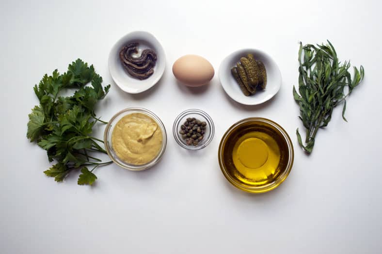 View of ingredients - dijon mustard, olive oil, egg, sardines, parsley, cornichons, capers and tarragon
