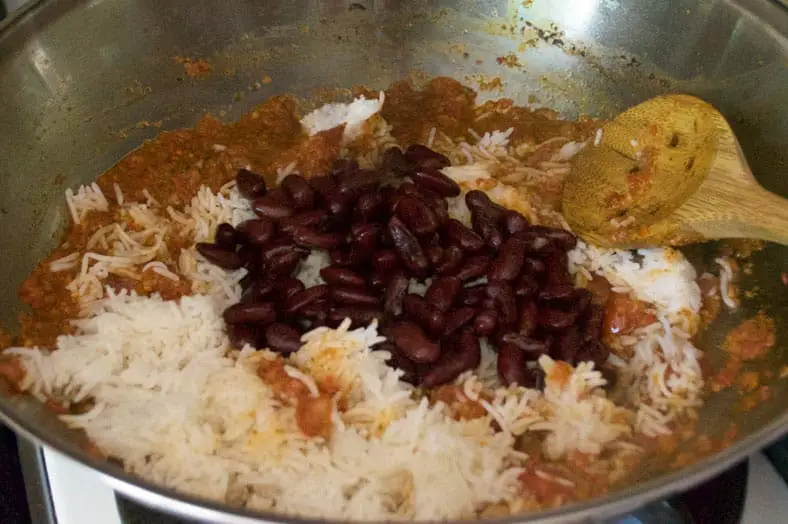 Adding beans and rice into a hot pan so the ingredients mingle together