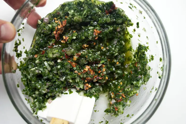 To make chimichurri, an Argentine sauce or marinade traditionally used on grilled meats, you'll need parsley, garlic, vinegar, olive oil and crushed red peppers at a minimum. Simply add the minced parsley, garlic, shallots, olive oil into a bowl and mix with a whisk or spatula. Then add the crushed red peppers and mix until evenly spread throughout the sauce.