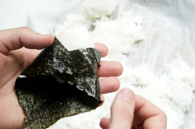 Once you've shaped your onigiri, cut a piece of your roasted seaweed and wrap it around your onigiri. It can be as much seaweed as to cover all the rice, or it can be as little as a strip of seaweed around. It’s completely up to you!