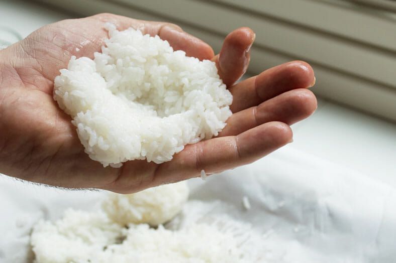 Start making your onigiri by taking a handful of your rice in the palm of your hand. To keep the rice from sticking to your hand, lightly wet your hands with water first. Then, create a small pocket in your rice for your filling.