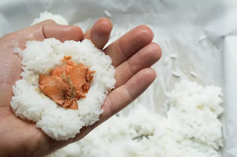 Start making your onigiri by taking a handful of your rice in the palm of your hand. To keep the rice from sticking to your hand, lightly wet your hands with water first. Then, create a small pocket in your rice and spoon some of your filling into the pocket.