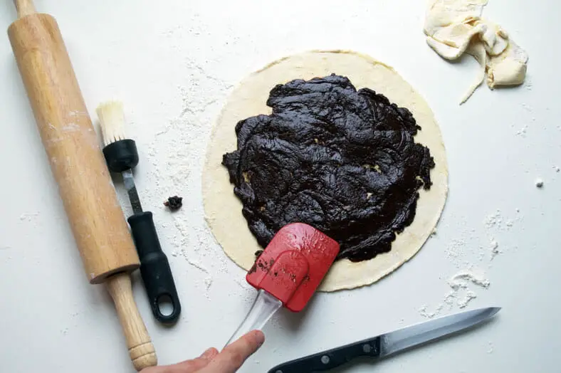With your rugelach pastry dough rolled out, take your filling and spread it evenly and smoothly across the surface area of your circular dough. You'll want to leave at least 1/2" of give between the circle's edge and the edge of your filling