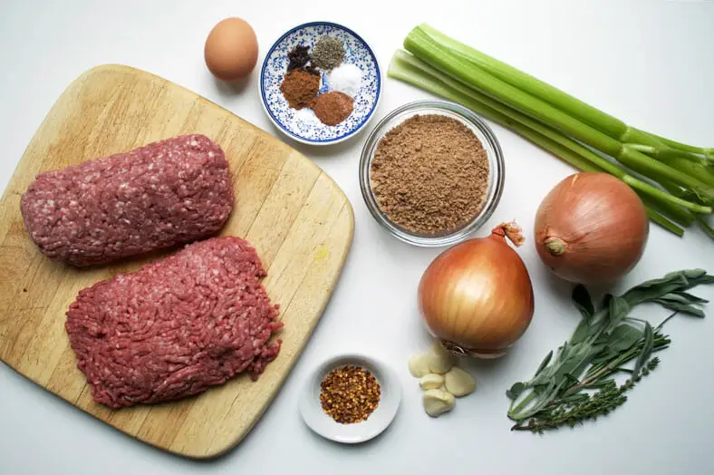 View of ingredients - ground pork, ground beef, onions, garlic, celery, nutmeg, cinnamon powder, spices, cloves, sage, thyme, and breadcrumbs