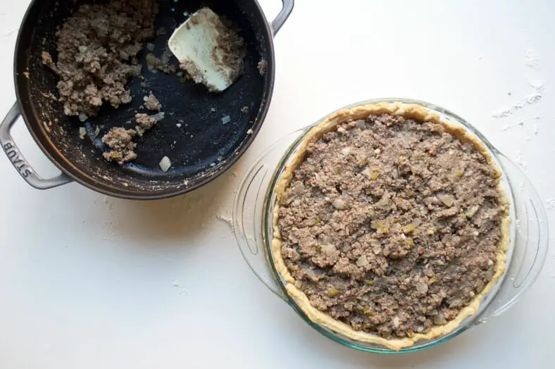 Filling the pie crust with meat filling in plate