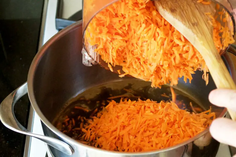 The first step to halva ye havij (Persian sweet carrot confection) is to soften and sweeten your grated carrots. You'll do this by dissolving sugar in water, then adding the carrots into that water