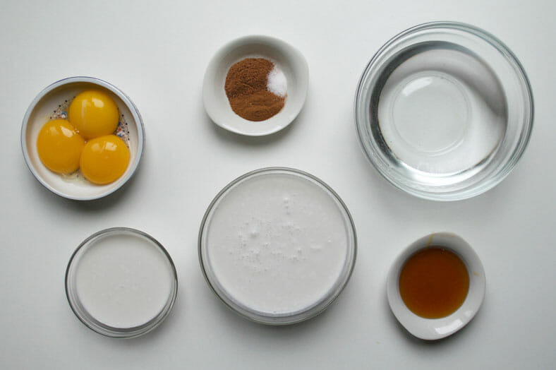 View of ingredients: egg yolks, rum, water, coconut milk, condensed coconut milk and vanilla extract.