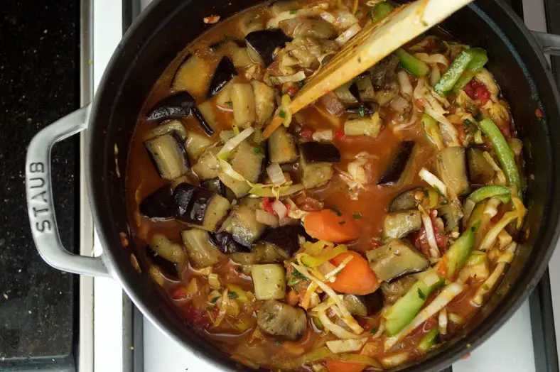 Adding broth to submerge all the vegetables, and again adding eggplant in to pot