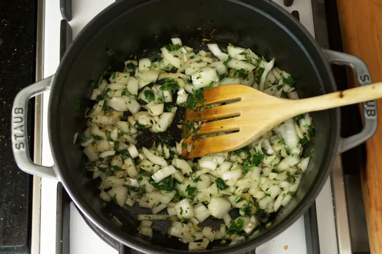 Adding chopped onions to parsley and ginger in pot