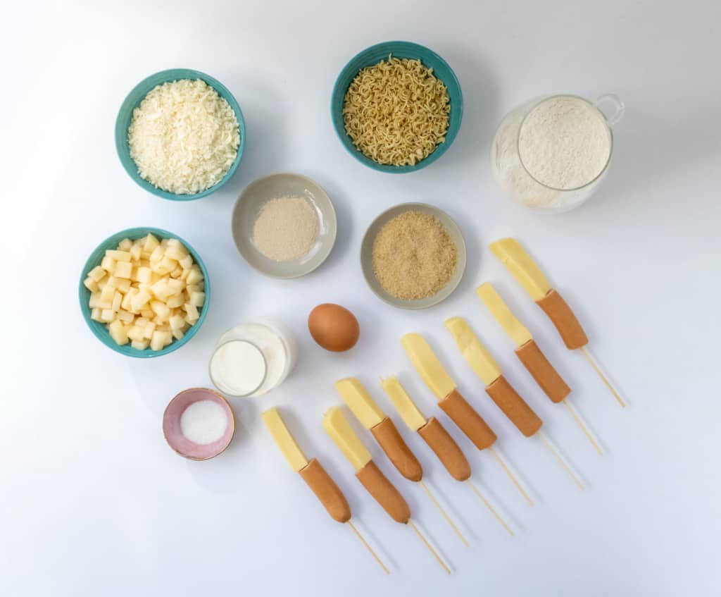 View of ingredients in bowls on a table - cheese, egg, yeast, hot dog stick