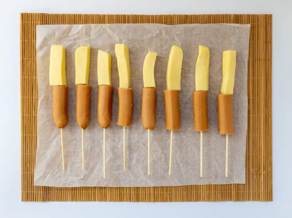 hot dog and mozzarella cheese sticks on skewers arranged on parchment paper