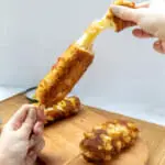 hand taking apart a korean corn dog with cheese on the inside